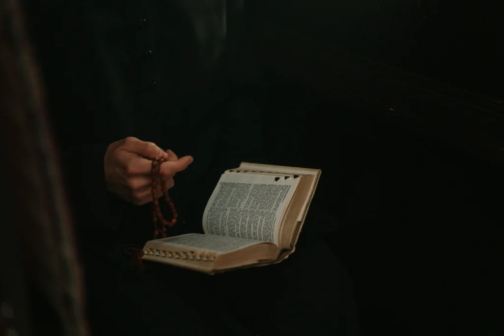The picture is dark, with only a person's hand and bible illuminated