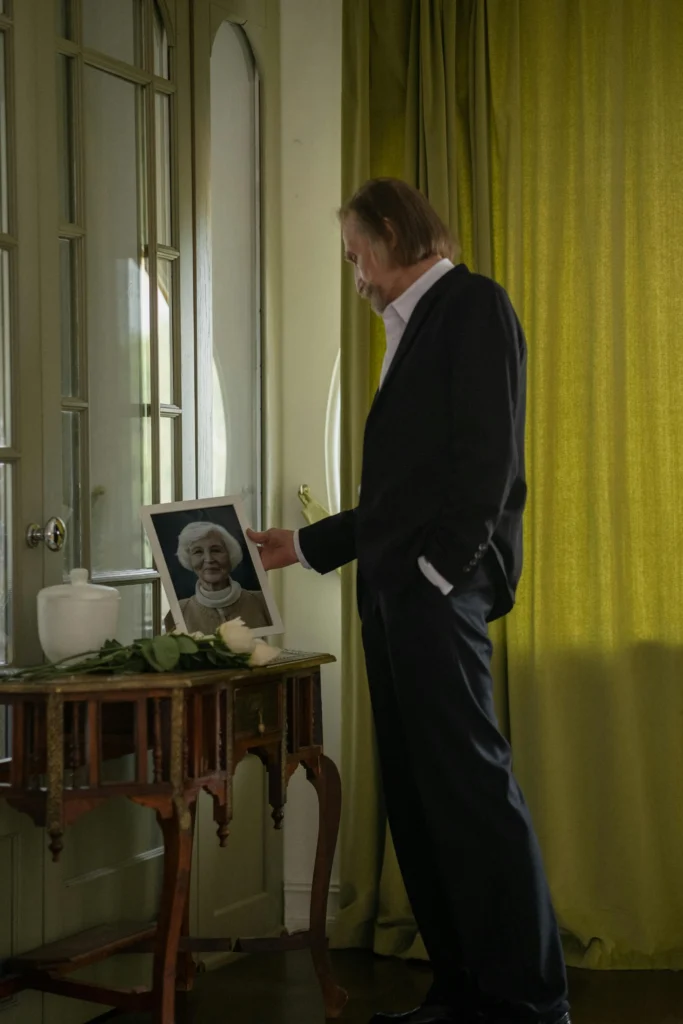 A man in a suit is touching a framed photo of an elderly woman.