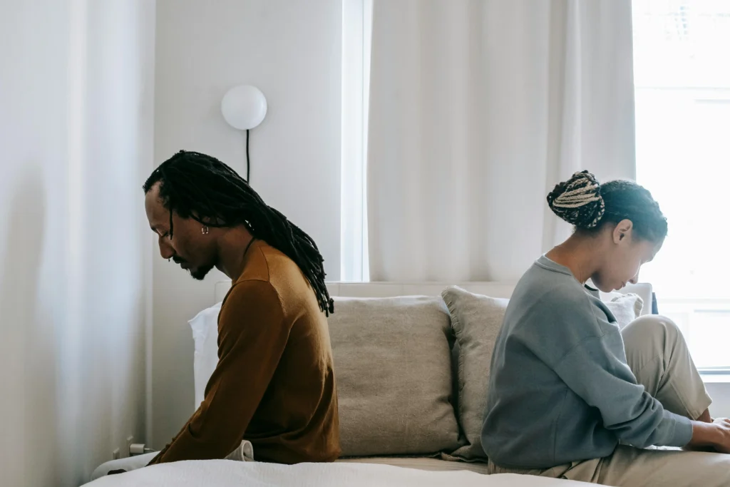 A man and a woman are sitting on opposite sides of a bed, backs facing each other.